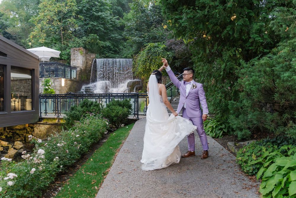 Candid wedding photo of groom twirling the bride along the path beside the waterfall at the ancaster mill.