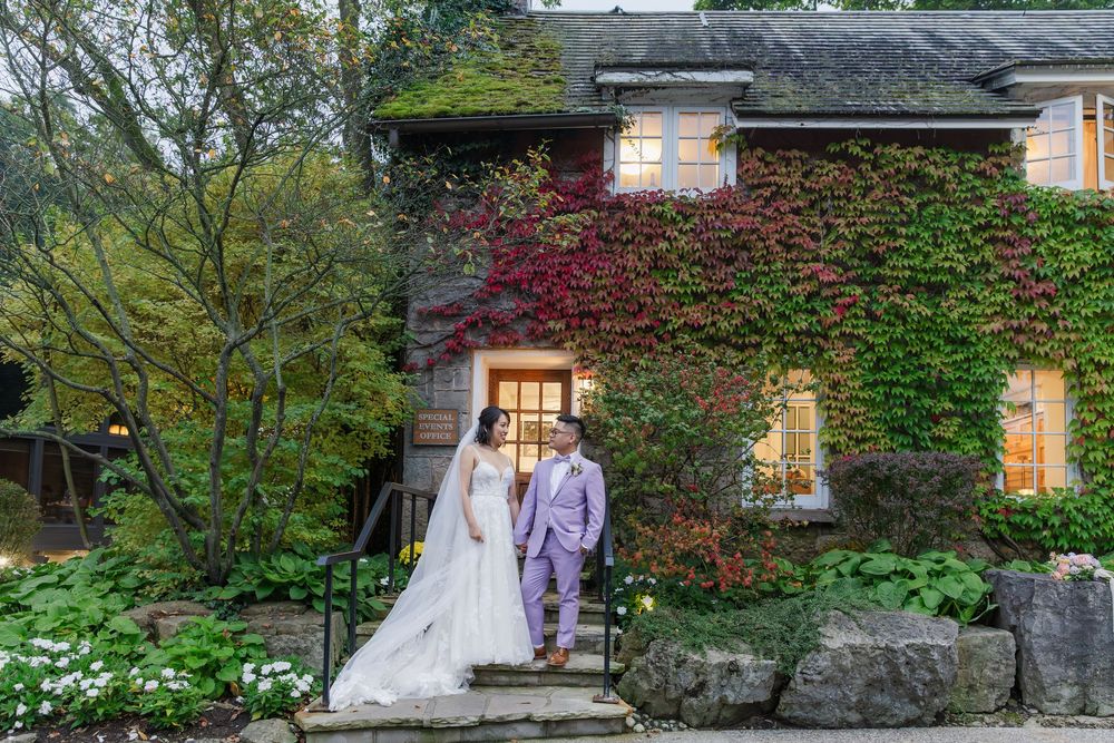 Bride and groom standing together in front of an ivy covered building at the ancaster mill during their wedding in hamilton, ontario.