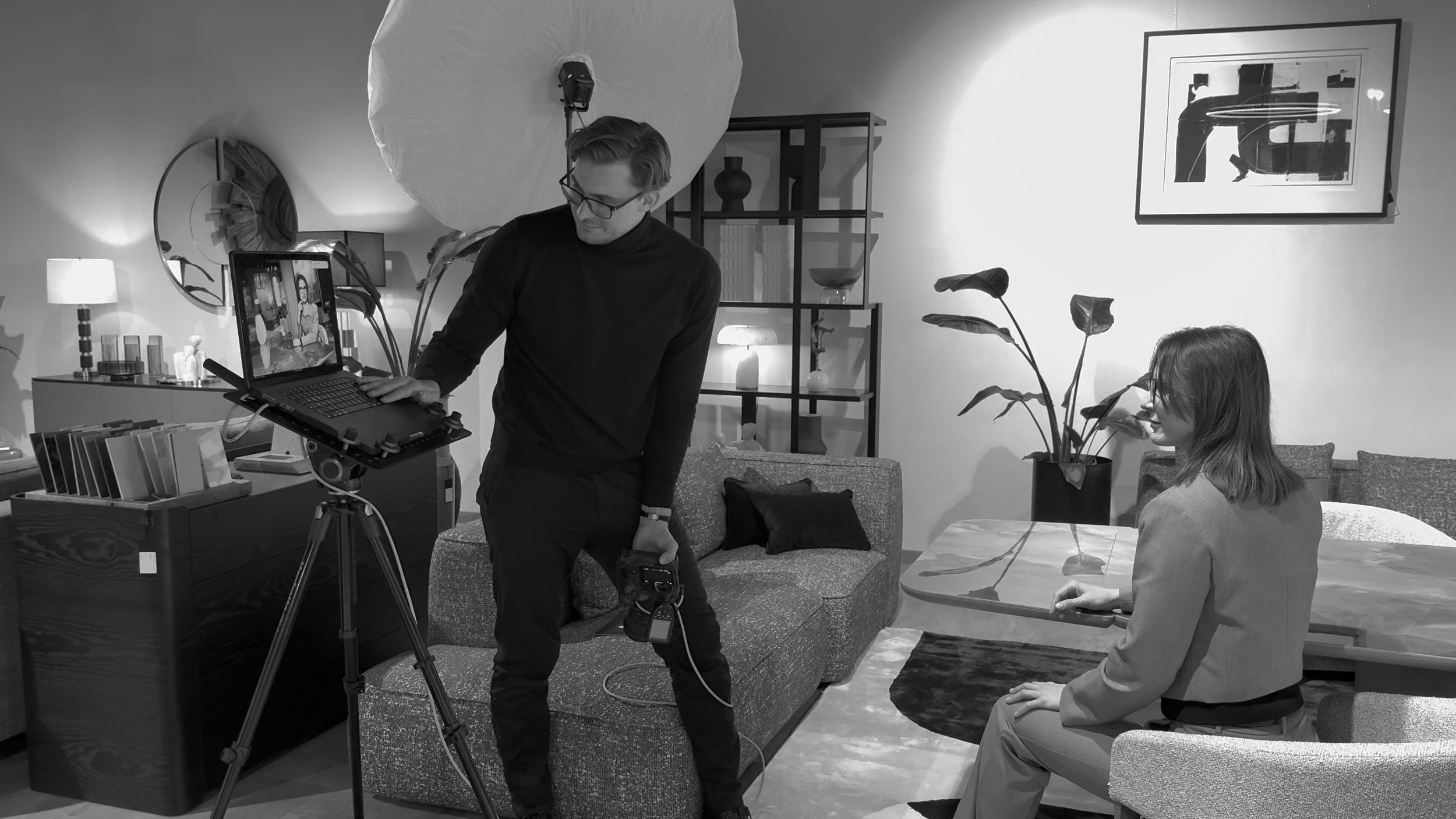 Czarno-białe zdjęcie biznesowej sesji fotograficznej w salonie meblowym z modelami, sprzętem oświetleniowym oraz krzesłami i sofami.