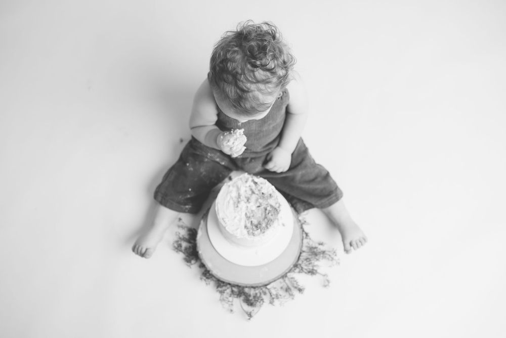 A baby sits on the floor surrounded by flour and cake during a messy cake smash photo session.