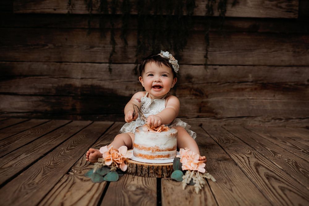 Small cake smash photography setup with rustic wooden floor and floral decorations.