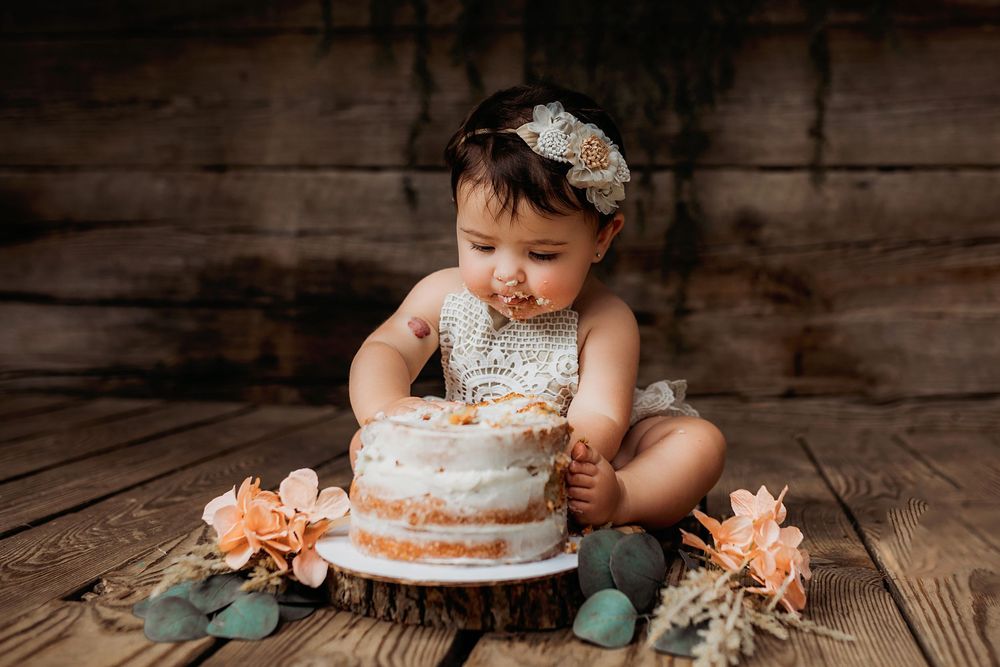 A rustic cake smash photography session features a white frosted cake on wooden floorboards.