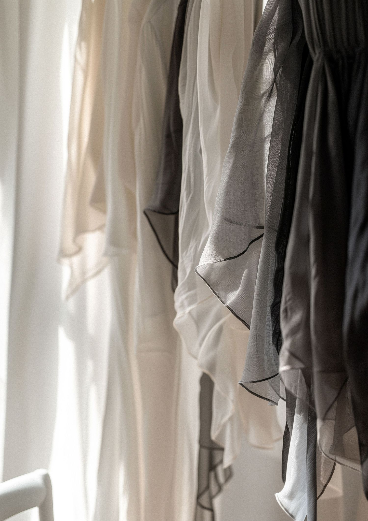 White robes and garments hanging on a clothing rack in a bright, sunlit room with elegant lace details.