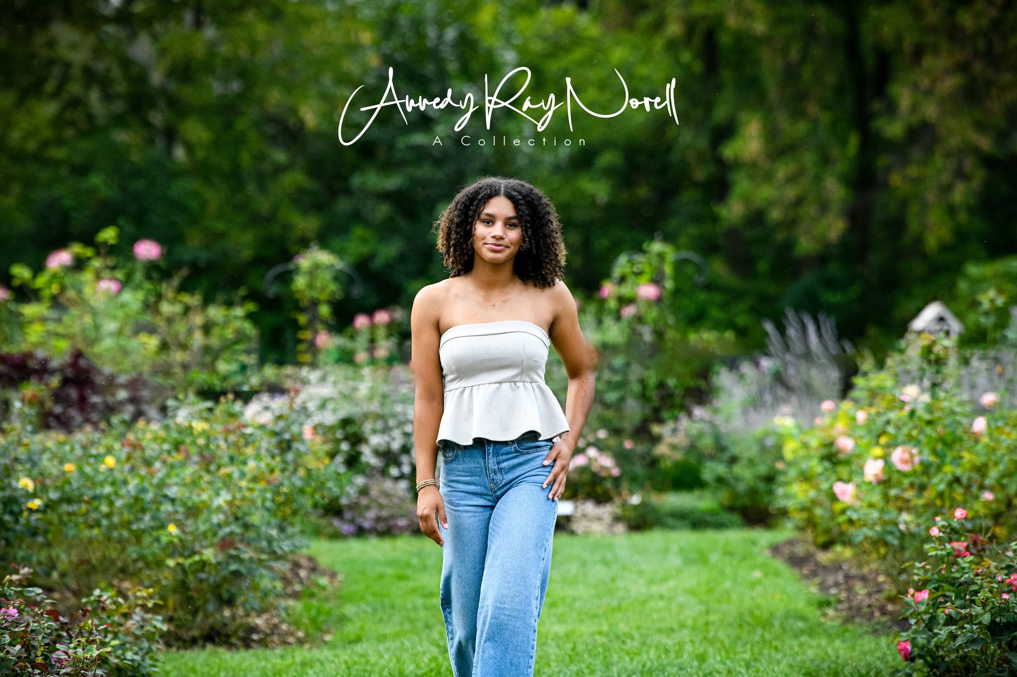 Young woman in white top and jeans walks through a lush garden filled with colorful blooming flowers.