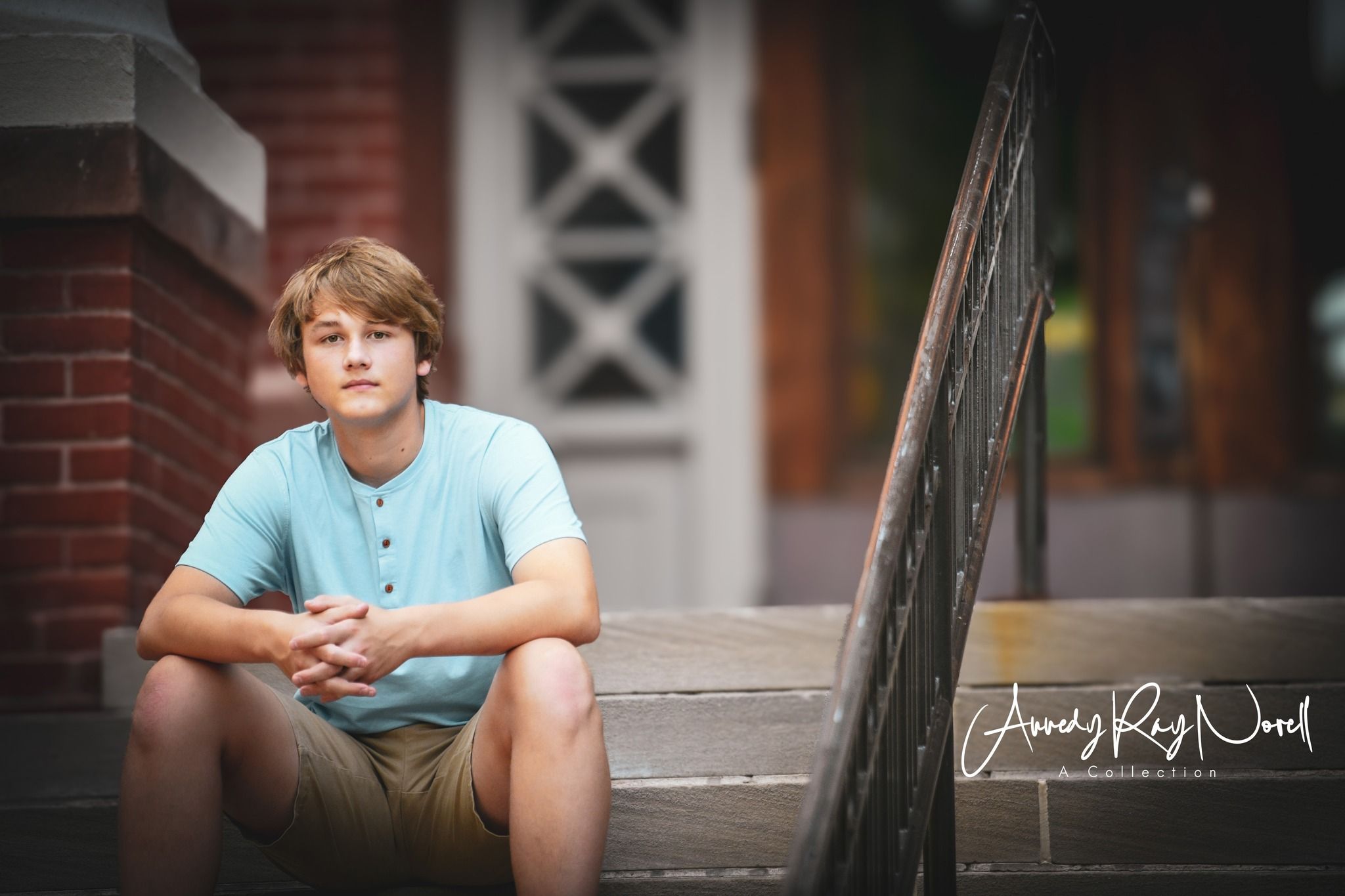 Teen boy in light blue shirt and khaki shorts sitting on brick steps during senior portrait photography session.