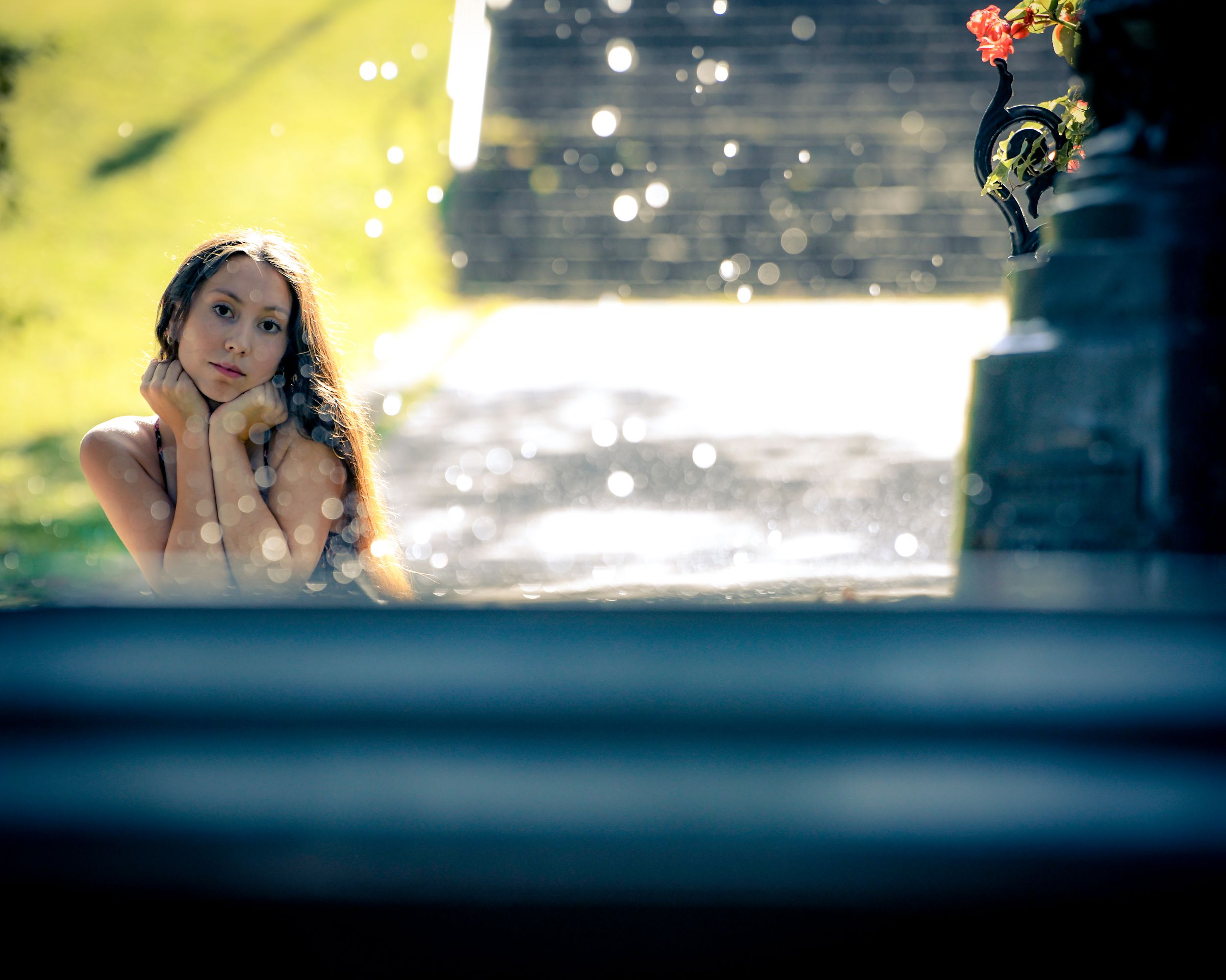Young woman resting her chin on hands, gazing thoughtfully outdoors near stone structure with bokeh light effects.