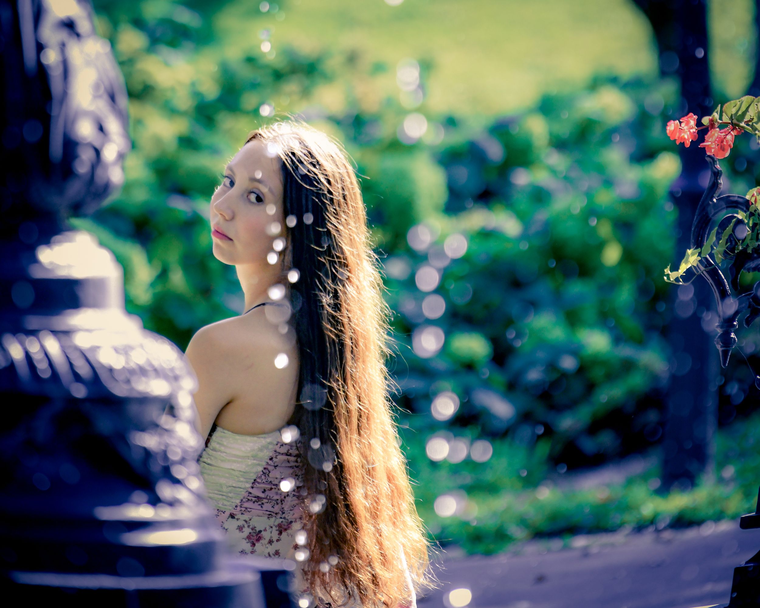 Young woman with long hair gazing upward in a dreamy bokeh-lit garden setting with soft light effects.