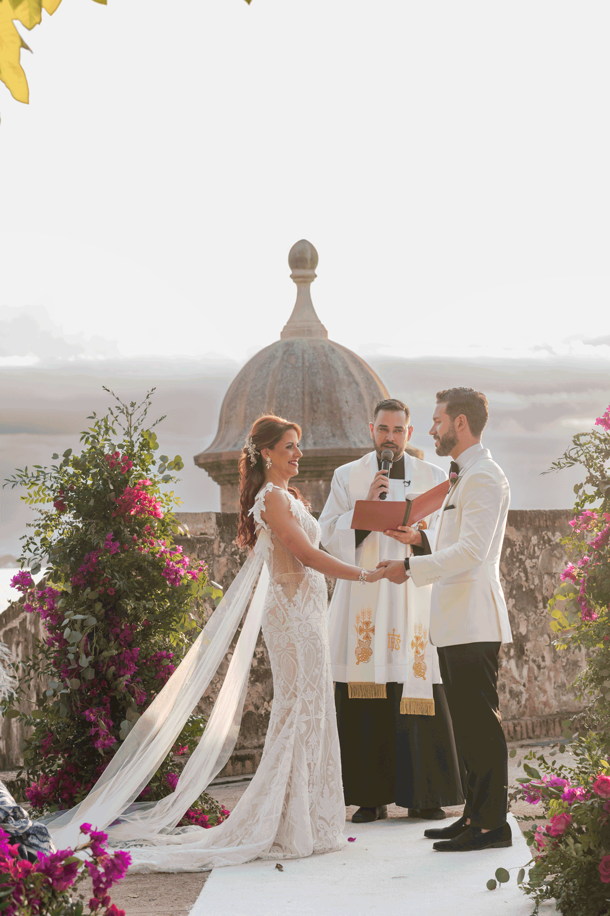 Wedding ceremony moment overlooking the ocean with floral arch and bride and groom exchanging vows