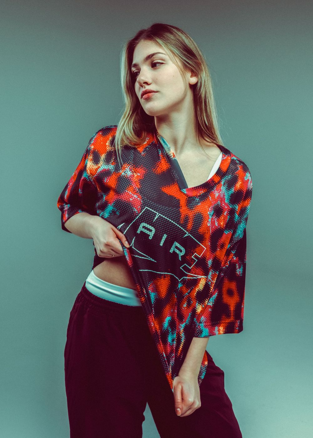 Young woman wearing a colorful Nike Air crop top with leopard print in red and teal, paired with dark velvet pants.