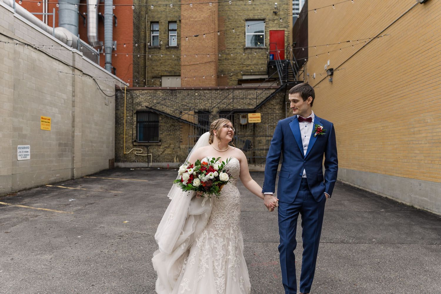 Candid wedding photo of bride and groom hold hands while walking in an alleyway across from the Walper hotel in Downtown Kitchener, Ontario.
