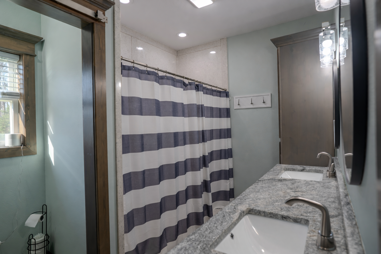 Modern bathroom with gray striped shower curtain, granite vanity countertop, undermount sink, and soft blue-gray walls.
