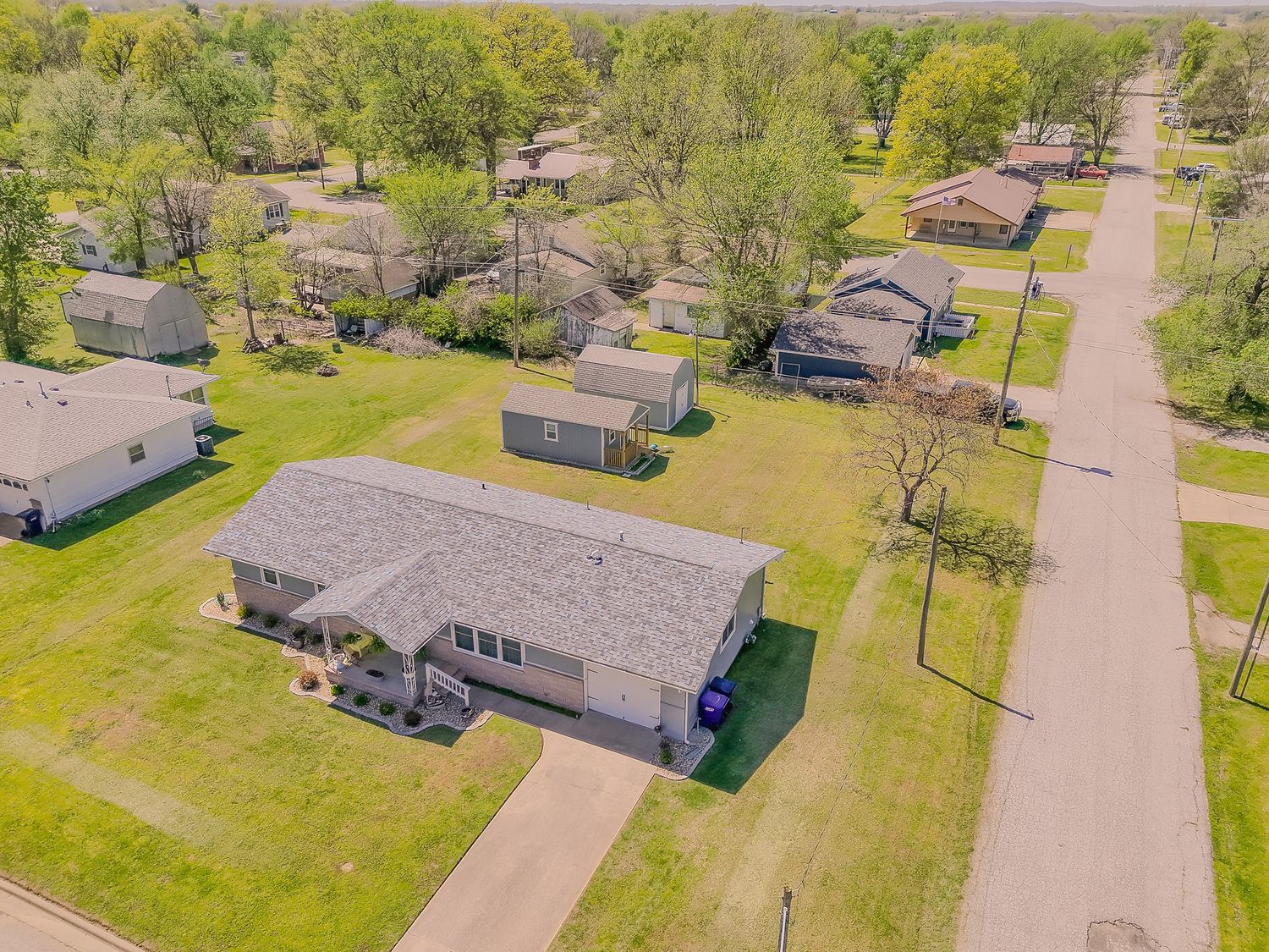 Aerial view of a suburban neighborhood with well-maintained homes, green lawns, and tree-lined streets on a sunny spring day.