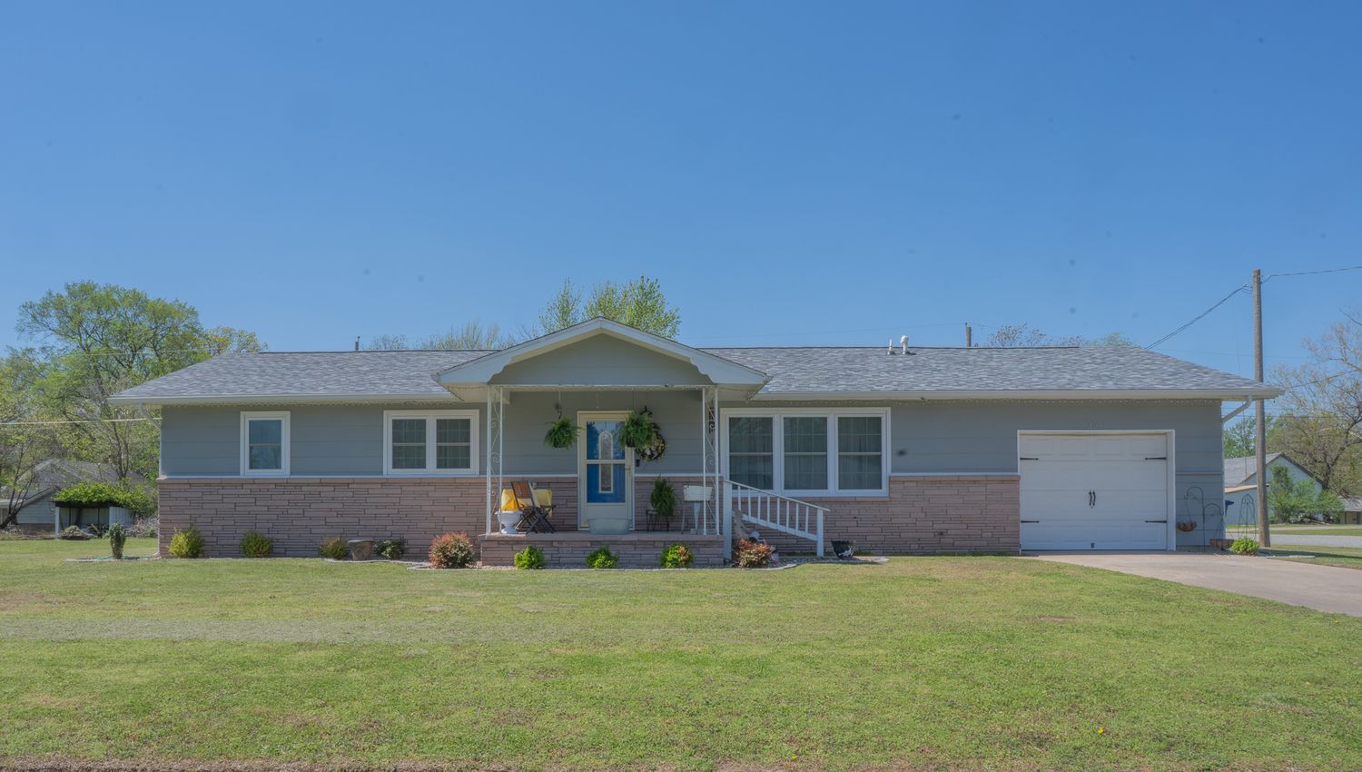 Ranch-style brick home with covered porch, attached garage, and lush green lawn on a sunny day.
