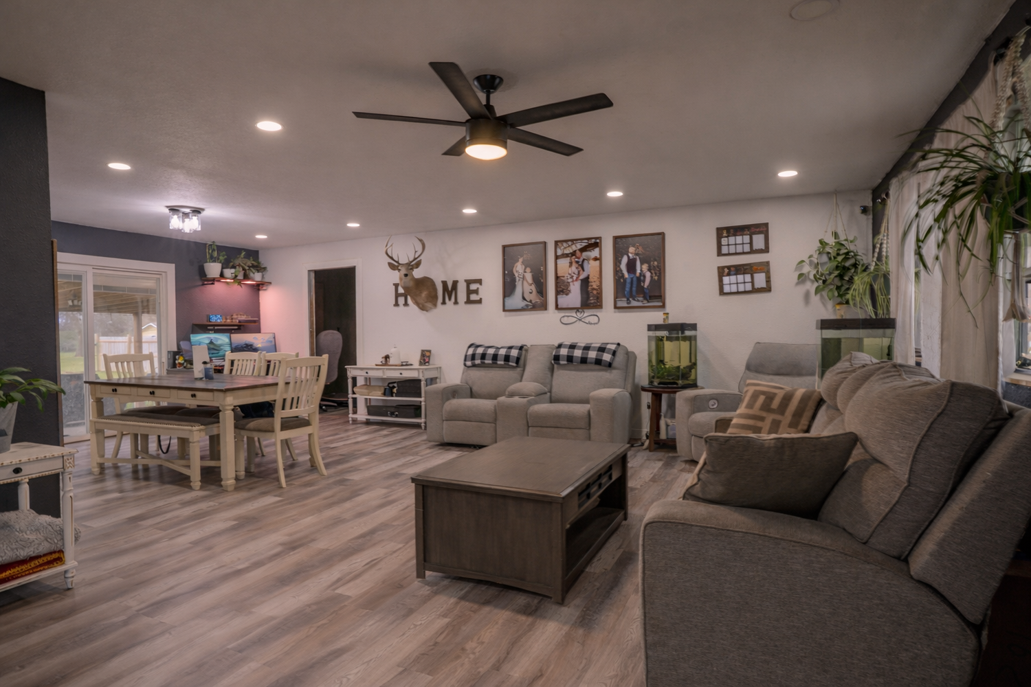 Cozy open-concept living room with gray sofas, wood coffee table, ceiling fan, hardwood floors, and HOME wall decor.
