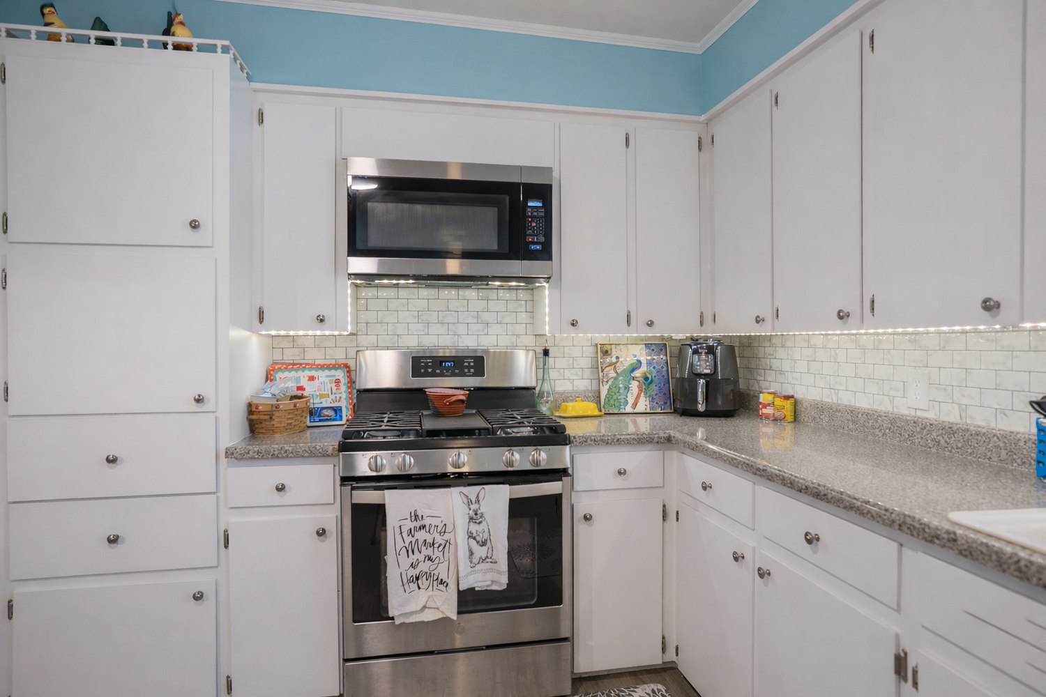 White kitchen with stainless steel stove, microwave, granite countertops, and subway tile backsplash.