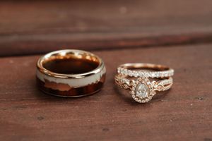 Rose gold wedding ring set featuring a pear-shaped diamond halo engagement ring paired with a wide tungsten wood inlay band.