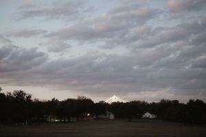 Cloudy dusk sky over a rural Texas landscape with trees and farm buildings silhouetted in the foreground.