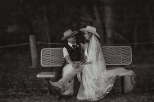 Black and white photo of a bride and groom in cowboy hats sitting on a bench, sharing an intimate moment.