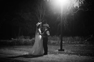 Black and white photo of a bride and groom in cowboy hats sharing a romantic moment under a street lamp at night.