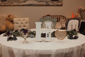Elegant wedding reception table with white linen, heart decor, floral arrangements, and decorative letter centerpiece.