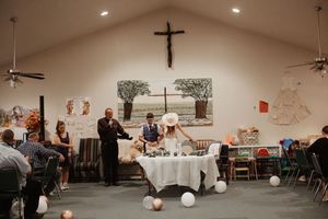 Wedding ceremony in a church with a cross, couple at altar, guests seated, balloons on floor, and decorative artwork on walls.
