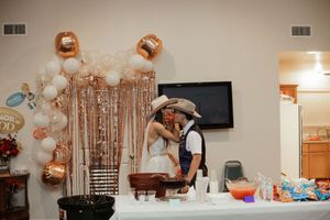 Couple in cowboy hats sharing a kiss at a party with rose gold and white balloon arch backdrop.
