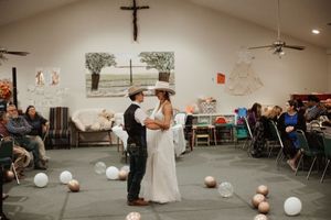 Bride and groom share first dance in rustic church wedding venue with balloon decorations and seated guests.