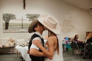 Couple sharing first kiss in cowboy hats at rustic country wedding reception indoors.