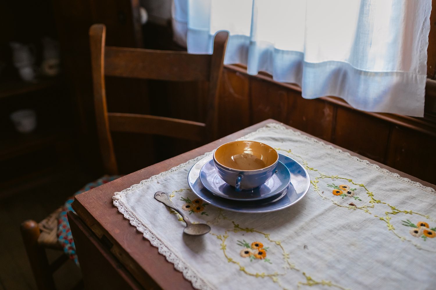 Vintage teacup resting on a delicate lace tablecloth with tiny orange and yellow flowers in low light at Canterbury Shaker Village in NH.