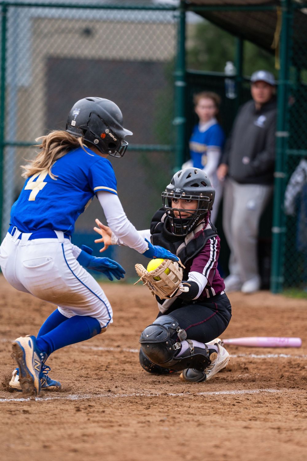 Bethel catcher tags out a blue-uniformed runner #4 at home plate during a softball game.