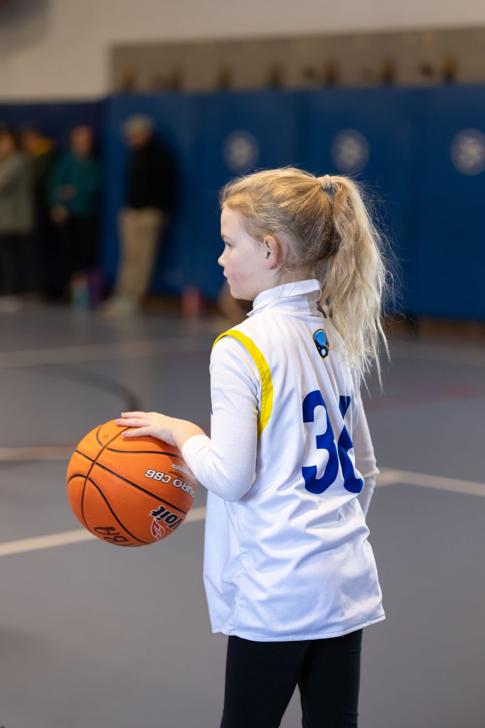 Young girl in white number 32 jersey holding a basketball on an indoor court during a youth game.