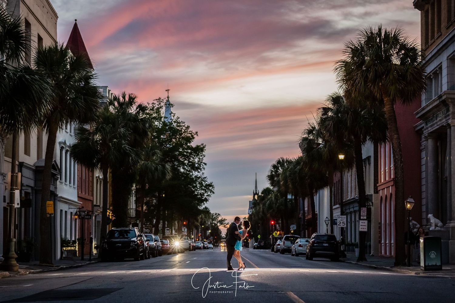 Couple embraces in the middle of a historic street at sunset with palm trees and colorful sky in Charleston, SC.