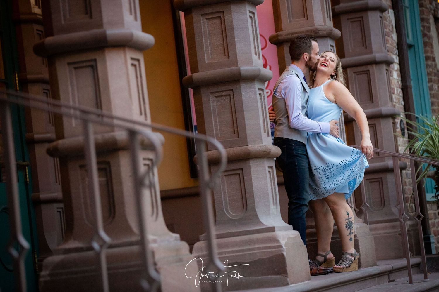 Couple sharing a romantic moment on urban brownstone steps, woman in blue dress, engagement photo session.