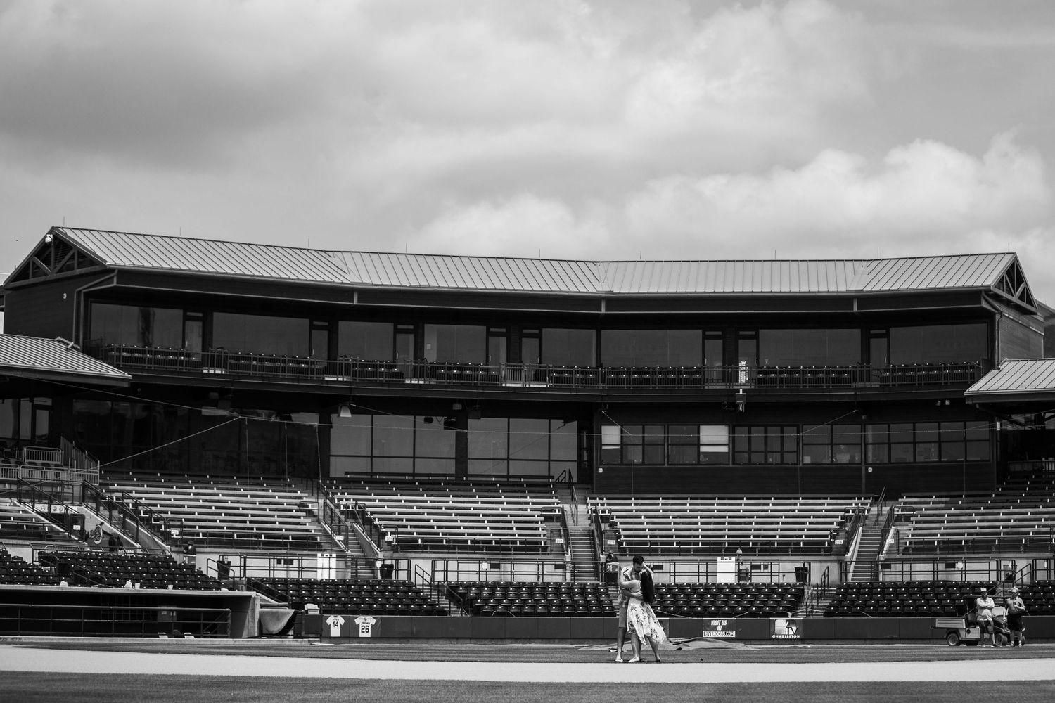 Black and white photo of an empty baseball stadium grandstand with tiered seating and a classic press box building.