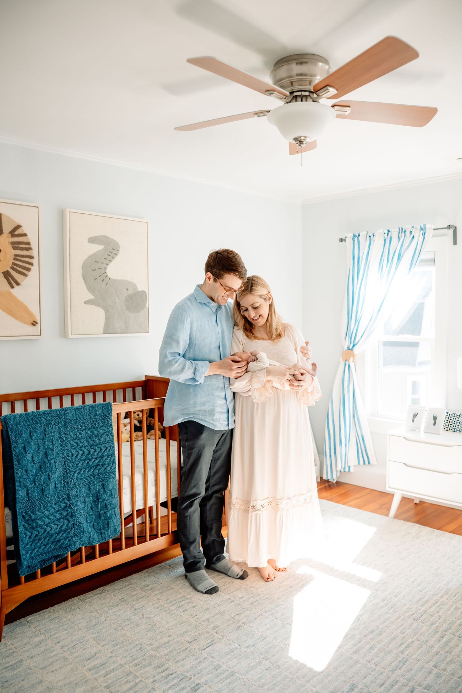 New parents stand together in a beautifully decorated nursery, tenderly cradling their newborn baby.