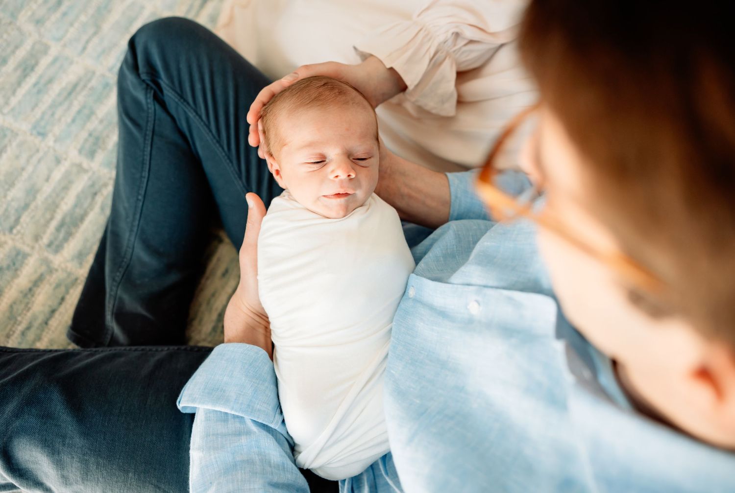 Parent cradling a sleeping newborn baby swaddled in white, sharing a tender bonding moment.