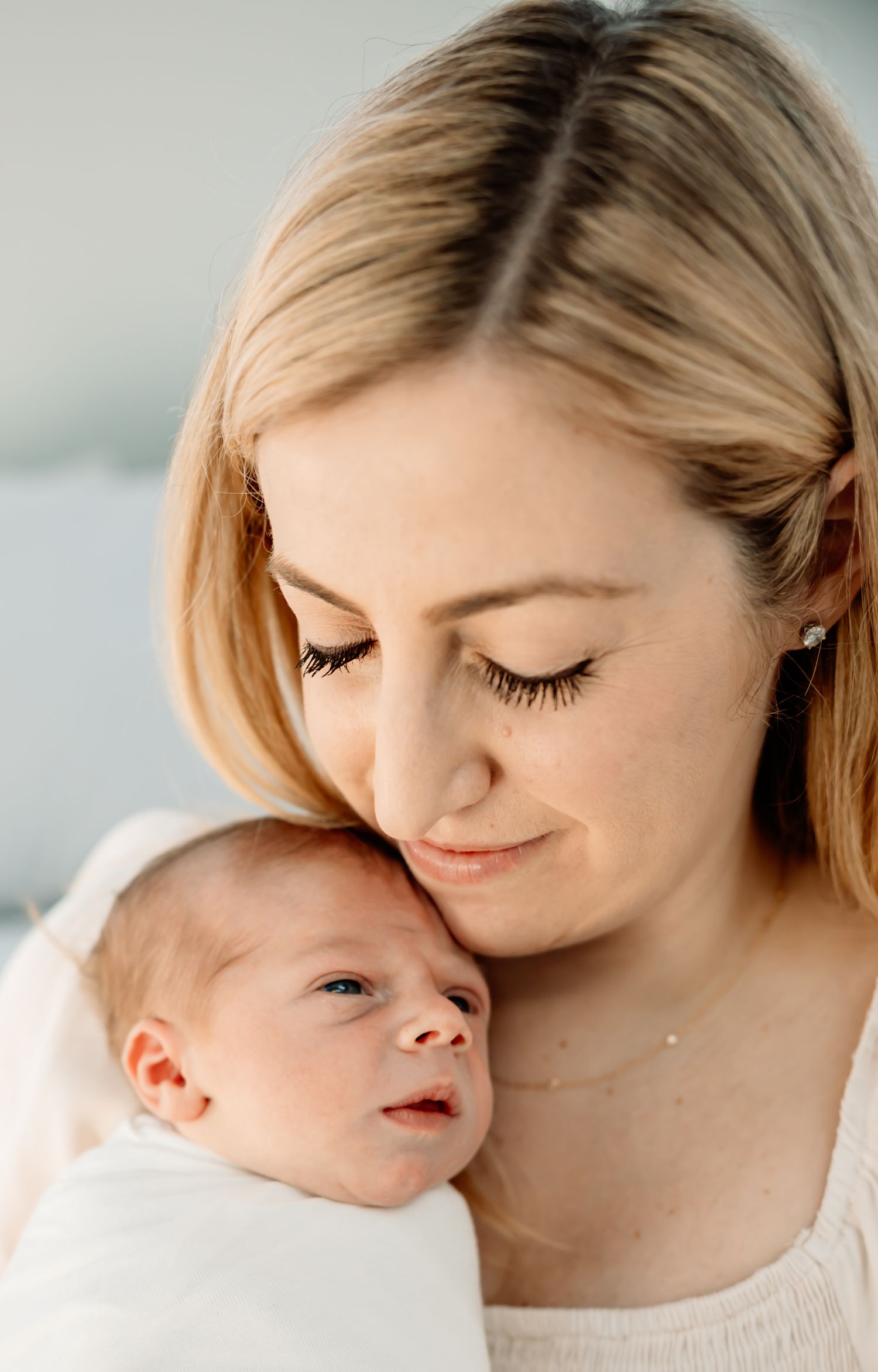 A blonde mother tenderly gazes down at her newborn baby, cradling the infant close to her cheek.