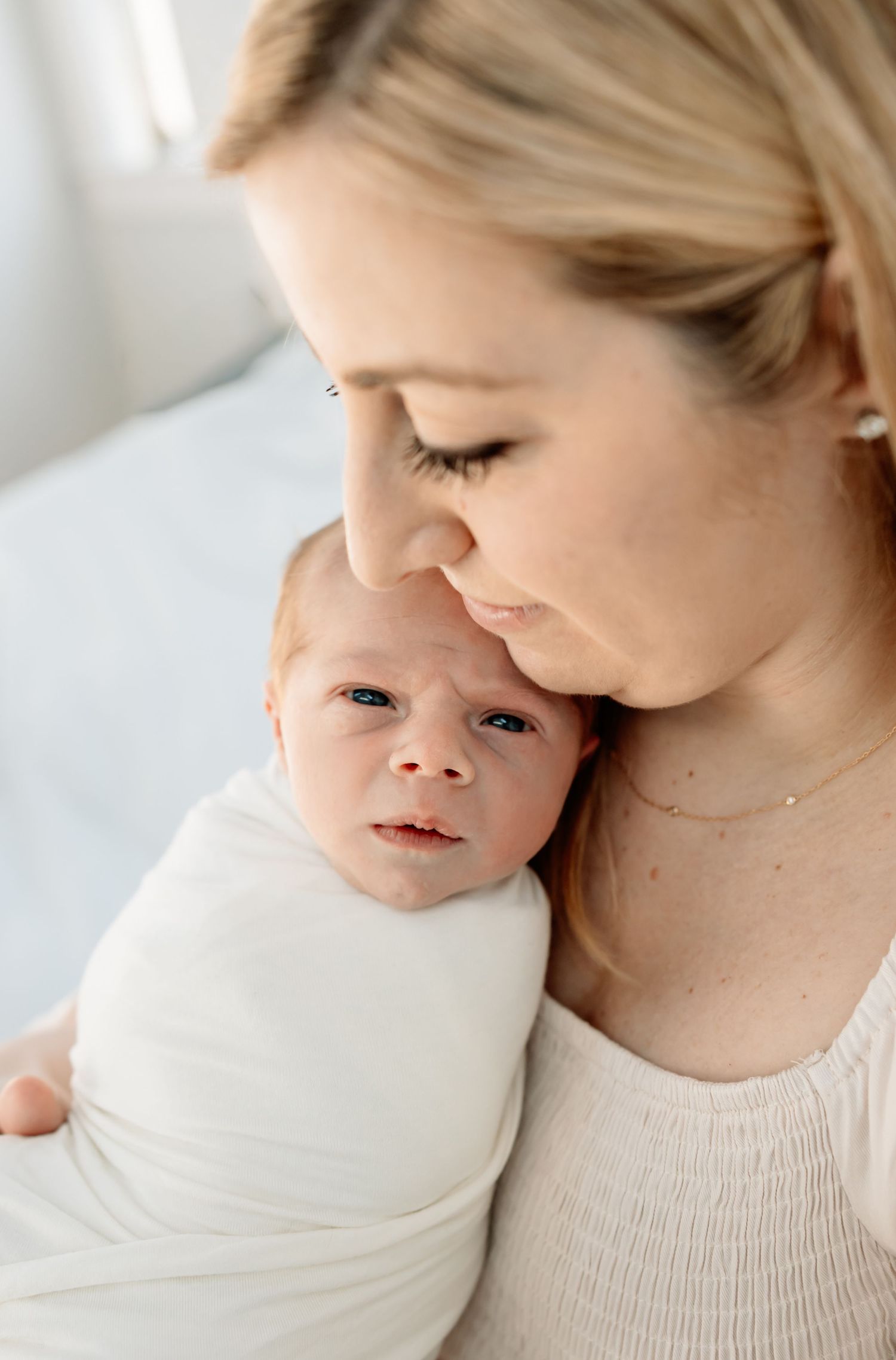 A mother gently nuzzles her swaddled newborn baby wrapped in white, sharing a tender moment together.