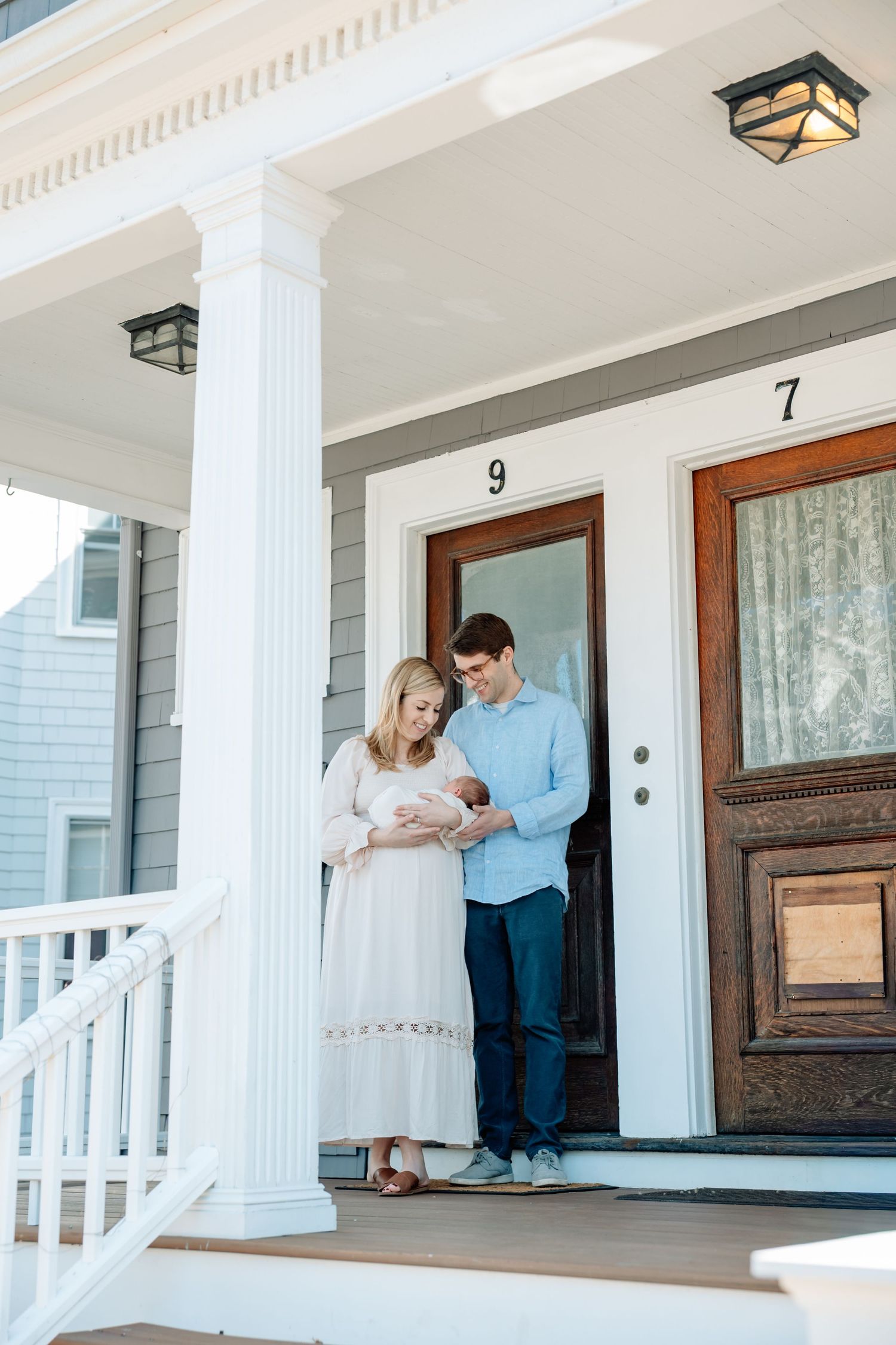 Happy new parents hold their newborn baby on a charming front porch of their home.
