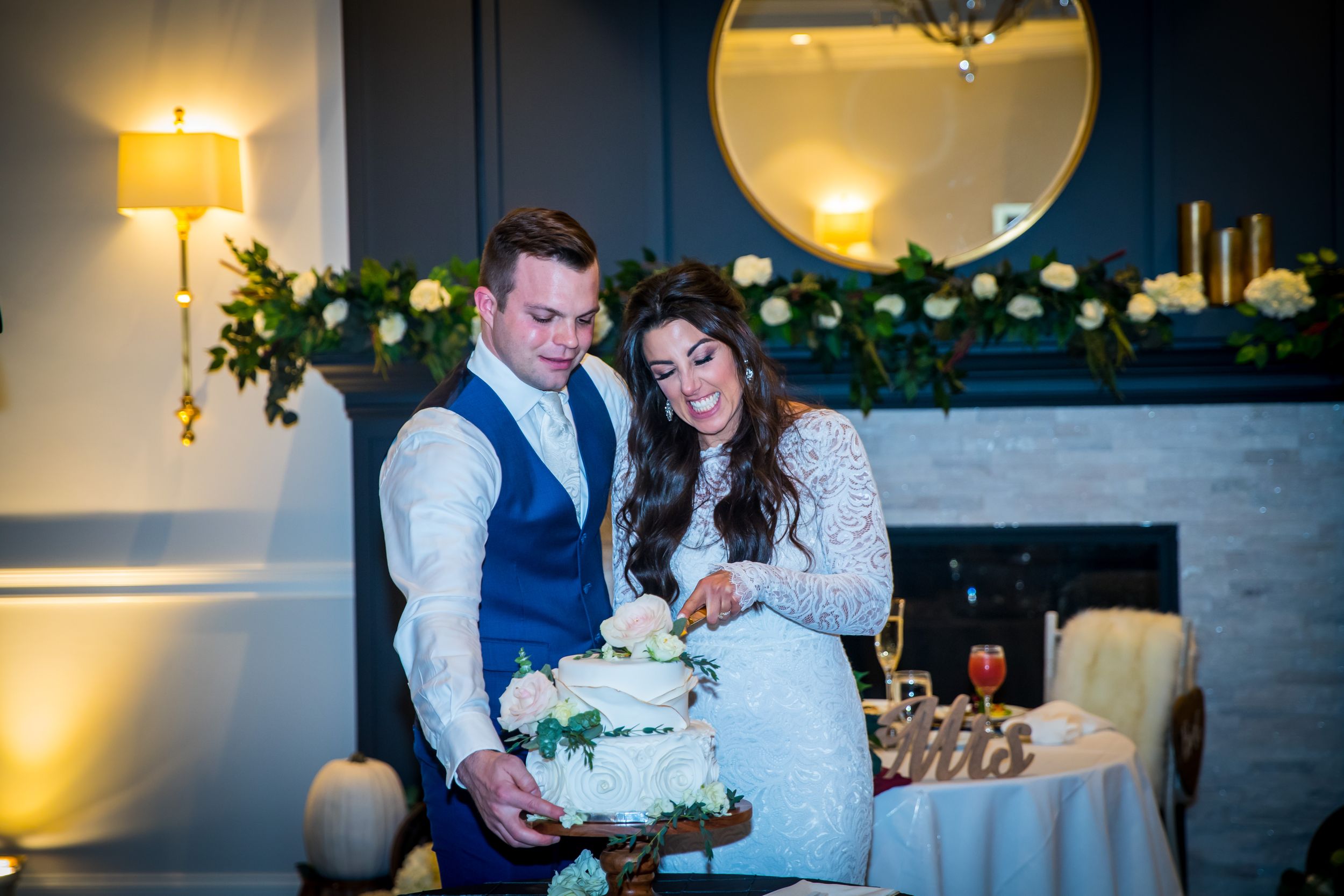 Bride and groom cutting their white floral wedding cake together in an elegantly decorated reception venue.