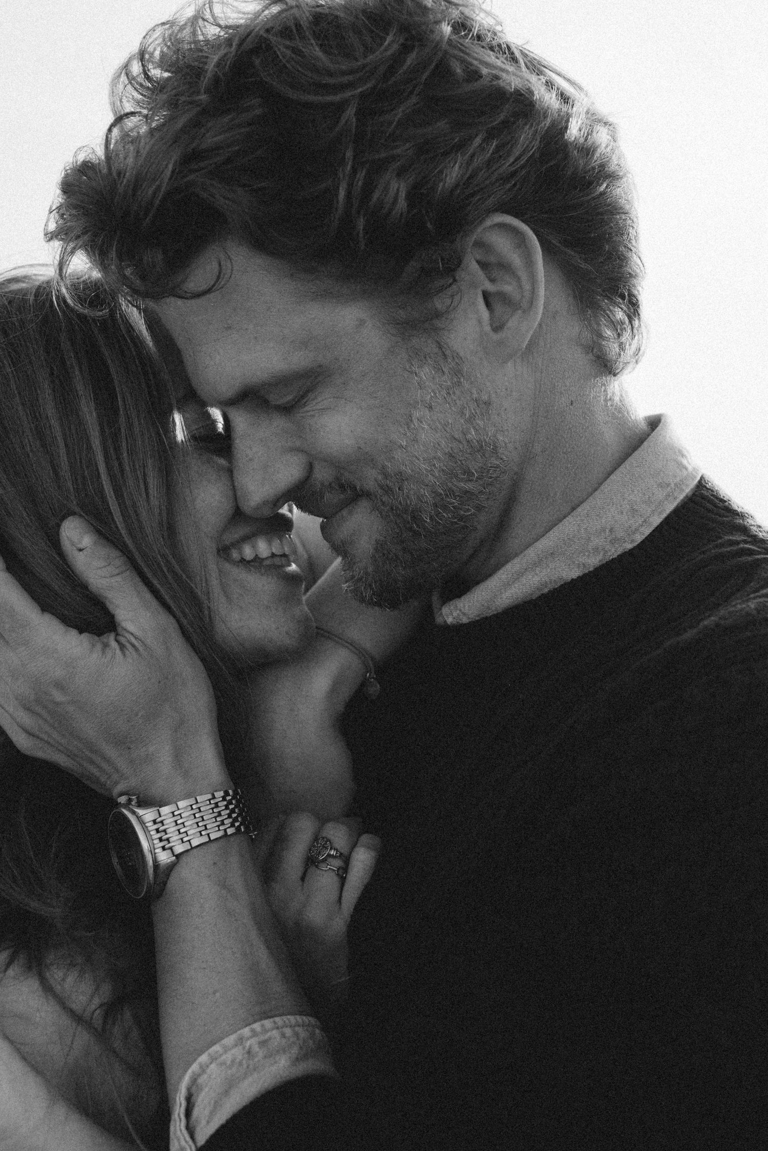 Black and white photo of a smiling couple sharing an intimate moment, the man tenderly holding the woman's face. Javea photographer