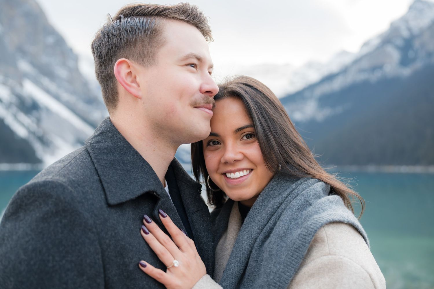 Couple embracing at Lake Louise, Canada, with snow-capped mountains in the background on a cold day.