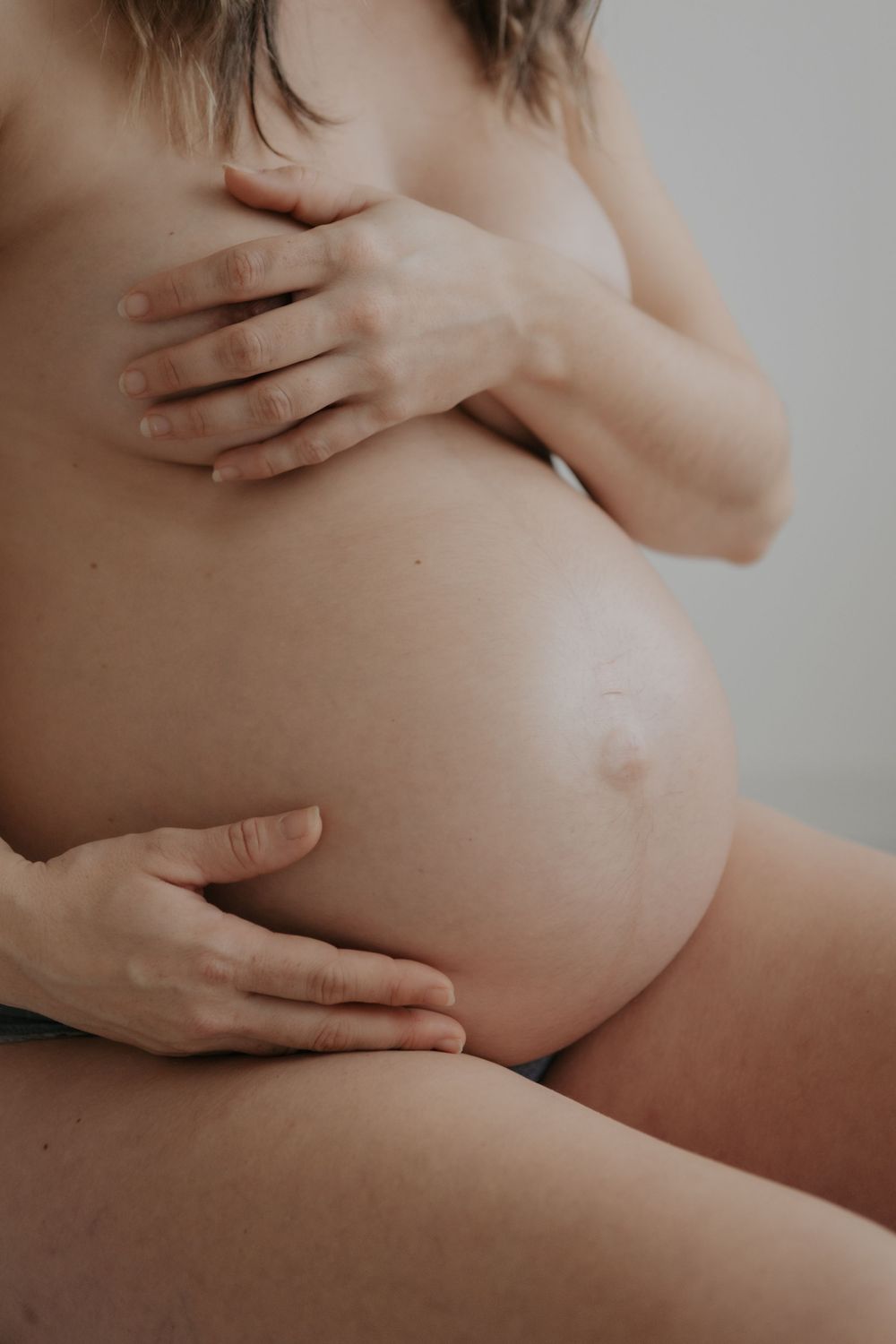 Close-up of bare pregnant belly with woman gently cradling bump with both hands. Cornwall Maternity Photographer