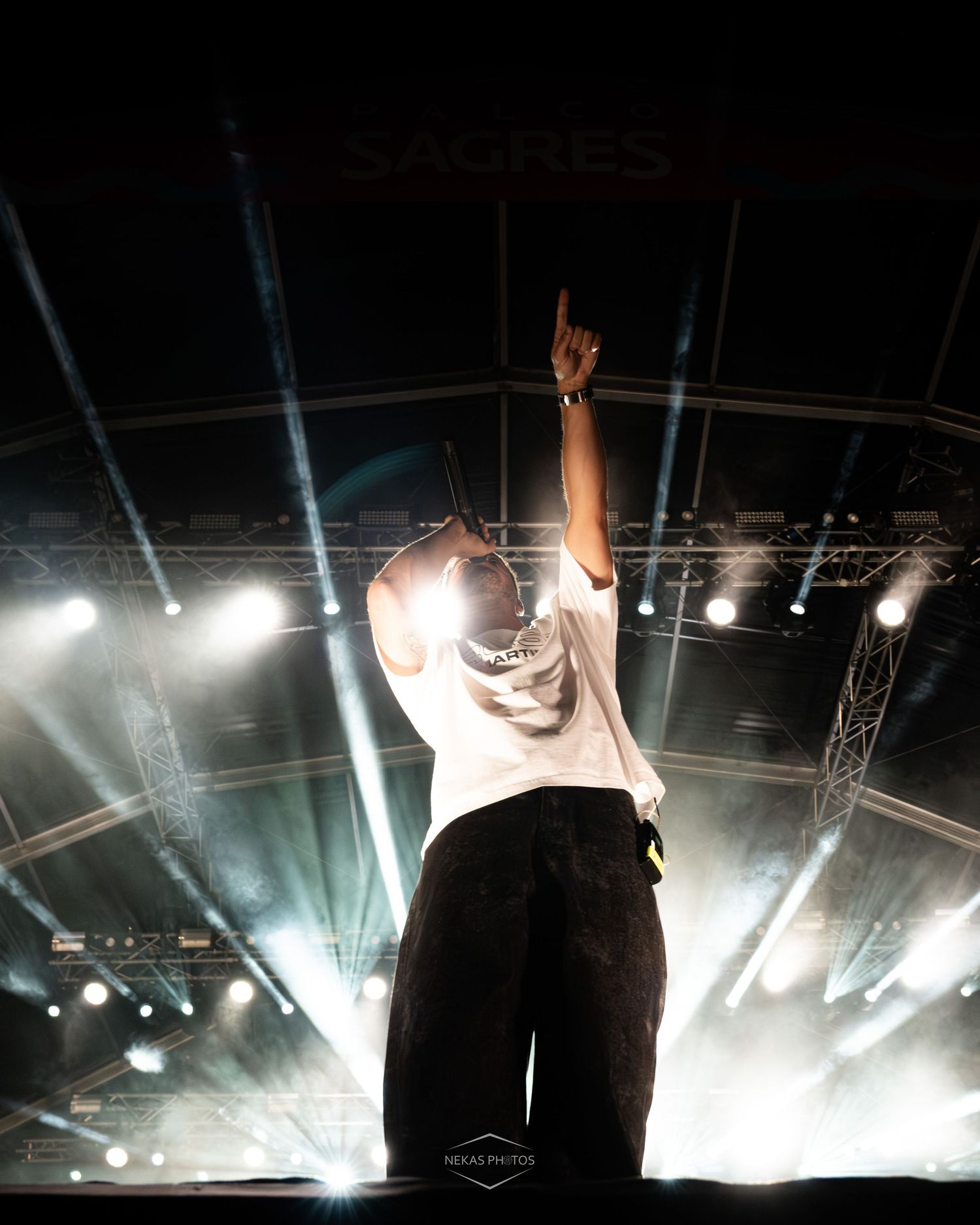 Performer on stage pointing up with dramatic stage lighting at a Sagres music festival concert.