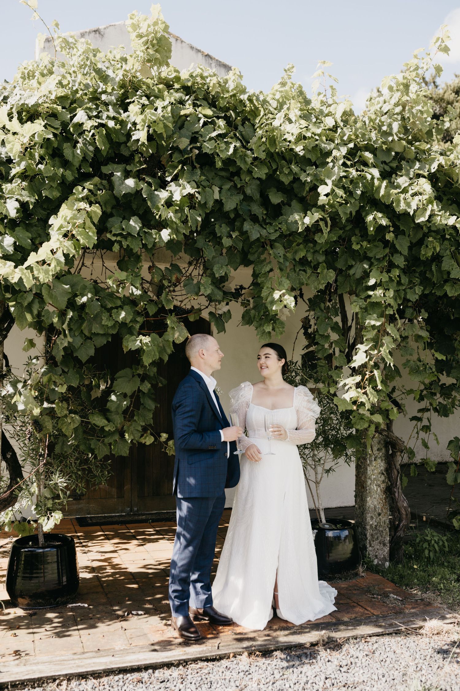 Bride and groom standing together under a lush green vine archway on their wedding day.