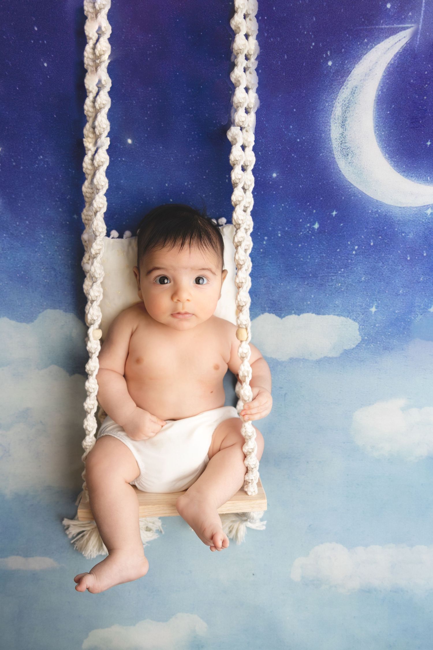 Adorable baby girl wearing a floral headband and purple vest, looking up with wide brown eyes and open mouth.