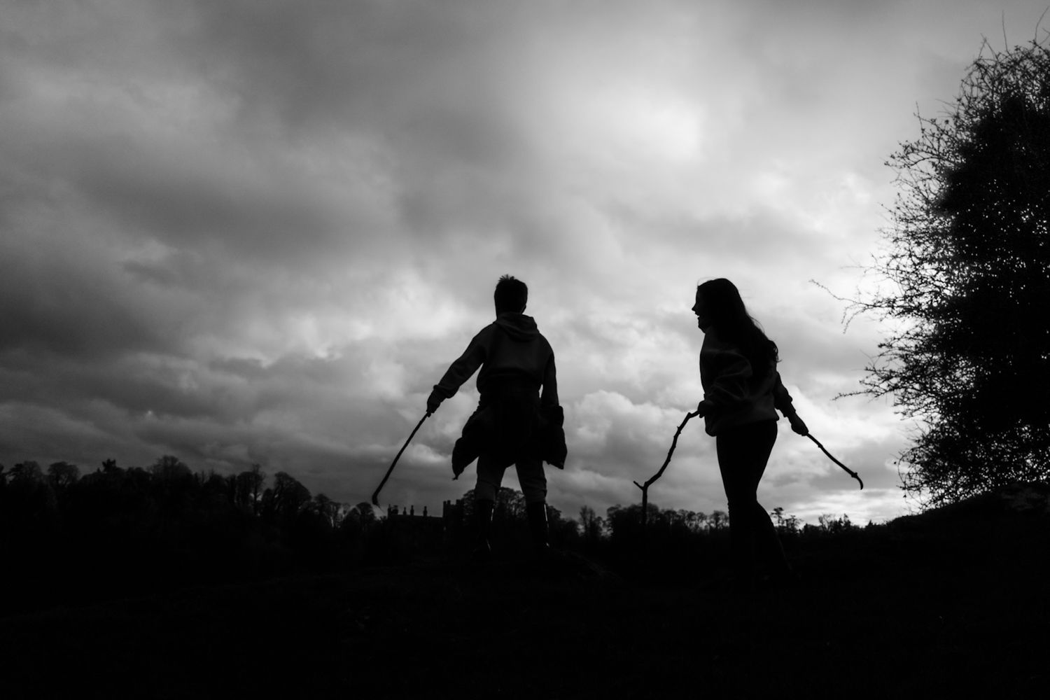 Silhouette of two people holding golf clubs against dramatic cloudy sky in black and white photography.