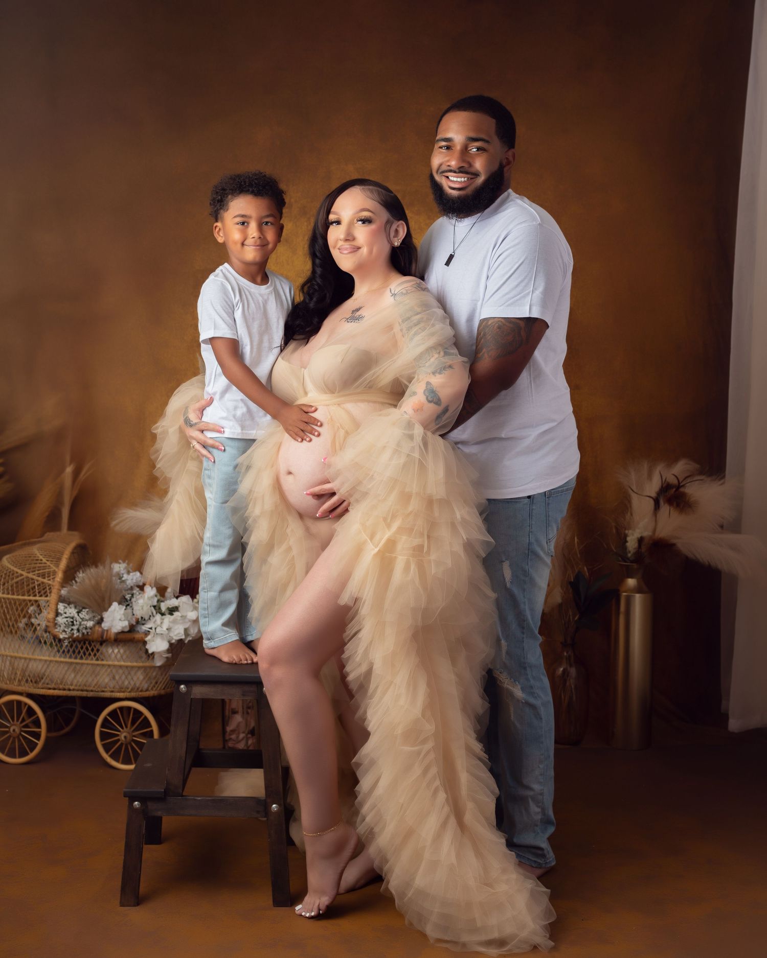 A pregnant mother in a white beaded bra necklace and silk fabric flowing bottom poses gracefully against a dark background.