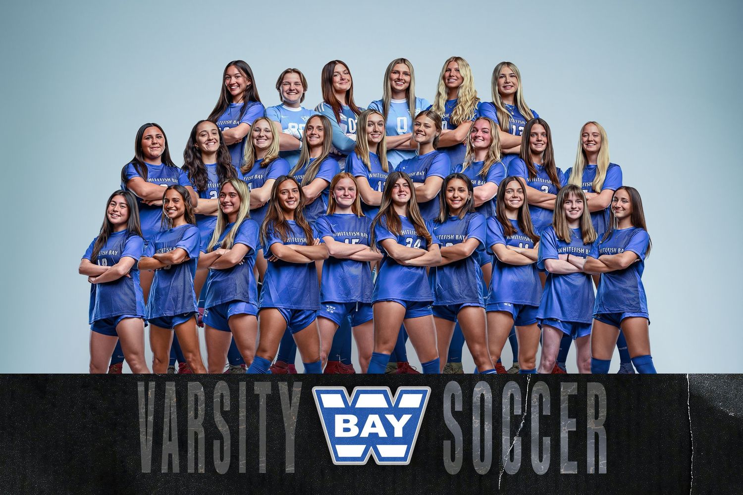 Varsity girls soccer team photo with players wearing blue uniforms posing in organized rows.