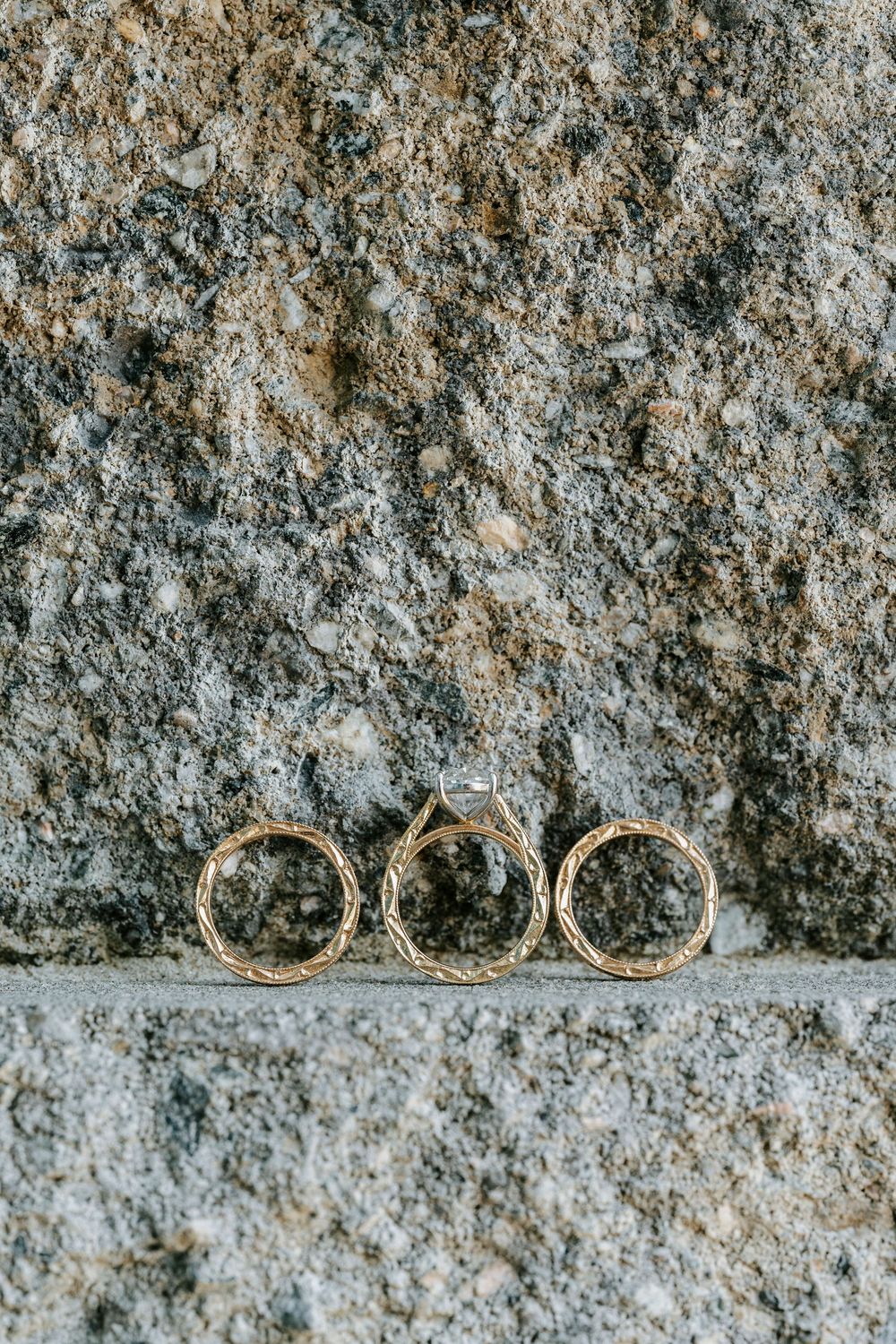 Three gold textured wedding bands leaning against a rustic granite stone wall.